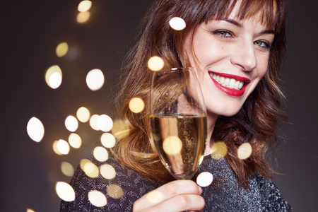 Woman wearing night party dress with a glass of champagne on dark background. Lady with long curly hair and perfect teeth celebrating and smiling.の写真素材