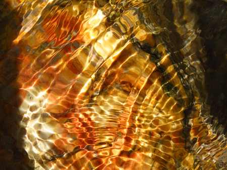 patterns of light and shadow reflected through water on a rockの写真素材