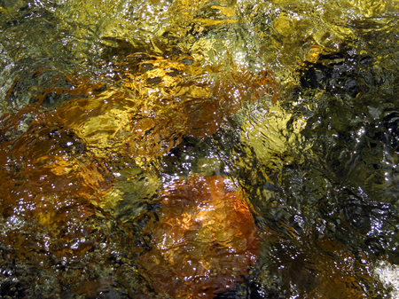 Water reflection on yellow green orange and black rocksの写真素材