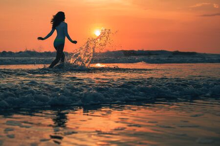 Silhouette of the woman running in the water during sunset.の写真素材
