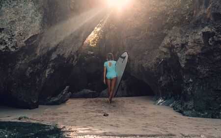 Beautiful young woman in bikini with surf board at beach of tropical island.