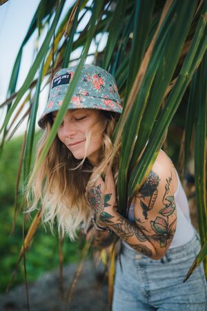 Portrait of beautiful young tattooed smiling woman standing in green leafy bushの写真素材