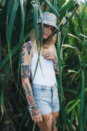 Portrait of beautiful young tattooed smiling woman standing in green leafy bushの写真素材