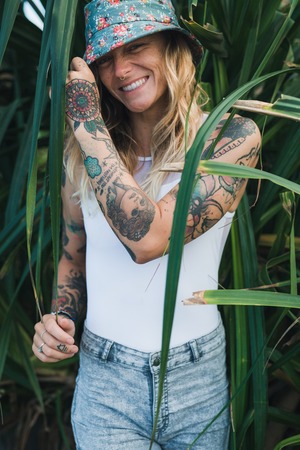Portrait of beautiful young tattooed smiling woman standing in green leafy bushの写真素材