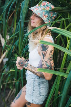 Portrait of beautiful young tattooed smiling woman standing in green leafy bushの写真素材
