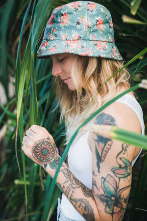Portrait of beautiful young tattooed smiling woman standing in green leafy bushの写真素材