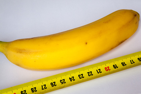 Diet concept. Banana with measuring tape closeup on white background