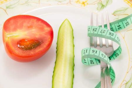 Cucumber and tomato with measuring tape over desk  - the concept of dieting and healthの写真素材