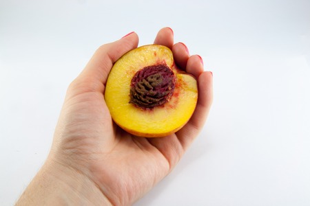 hand with a fresh juicy peach split in half isolated on a white backgroundの写真素材