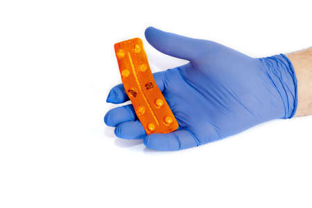 male hand in a blue glove holds an orange blister with pillsの写真素材
