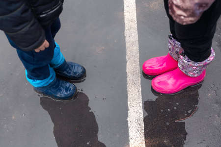 Two children wearing red rain boots jumping into a puddle. Close up. Kids having fun with splashing with water.の写真素材