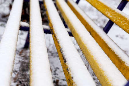 Yellow bench is covered with the first white snow. The beginning of winter after autumn.の写真素材