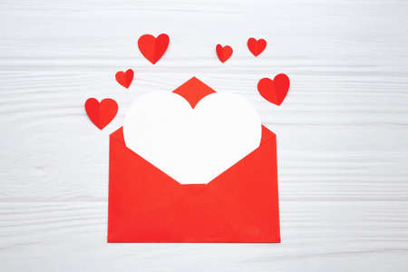 Red envelope with a white sheet of paper and red hearts on a white wooden background. Valentine's day greeting card.の写真素材