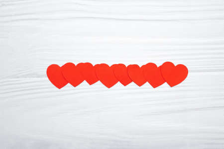 Red paper hearts hanging on white wooden background. valentines day