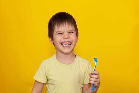 Happy toddler boy brushing his teeth with a toothbrush on a yellow background. Health care, oral hygiene. A place for your text.の写真素材