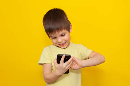 Little kid playing games on smartphone over yellow background. The concept of modern education. copyspace,の写真素材