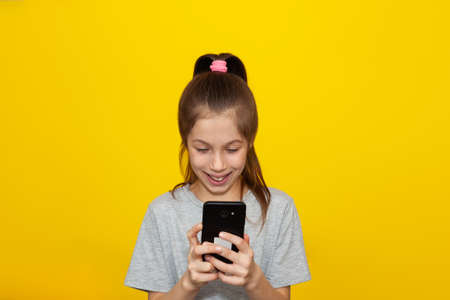 Cute little girl playing smart phone and smiling, standing over pastel yellow wall. copyspace. The concept of modern education. remote learningの写真素材