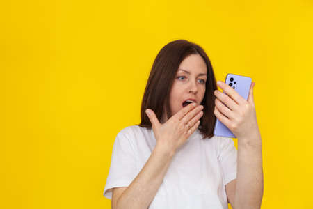 Portrait of a smiling european brunette woman wearing white T-shirt on yellow background talking on...