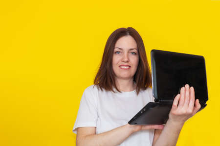 Portrait of a woman in a white t-shirt with a laptop on a yellow background. Business woman working with laptop at home. The concept of remote work or online learningの写真素材
