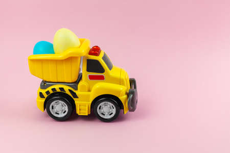 A toy yellow truck carrying Easter eggs in pastel colors. Easter card with place for text on a pink background. Easter food deliveryの写真素材
