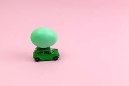 Toy green car with Easter egg on the roof. Easter card with space for text on a pink background....