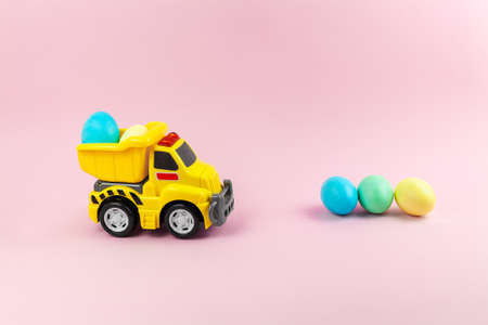 A toy yellow truck carrying Easter eggs in pastel colors. Easter card with place for text on a pink...
