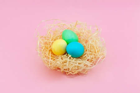 Easter eggs painted in pastel colors in hay nest against a pink background, copyspace for Happy Easter textの写真素材