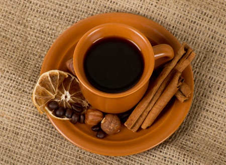 Closeup shot of freshly prepared cup of italian espresso with cinnamon, coffe beans, nuts and lemon over sackingの写真素材