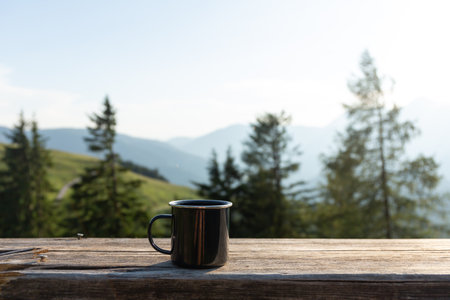 Tin mug on the wooden bench on the mountains background. Hiking conceptの写真素材