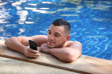 young handsome man with a phone in the poolの写真素材
