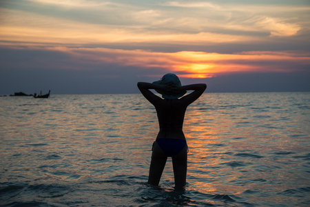 girl looks at sunset on the beach in thailandの写真素材