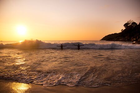two men are floating on waves in the sea at sunsetの写真素材
