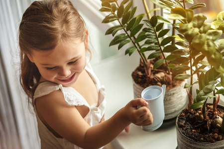 little girl watering and caring for house plantsの写真素材