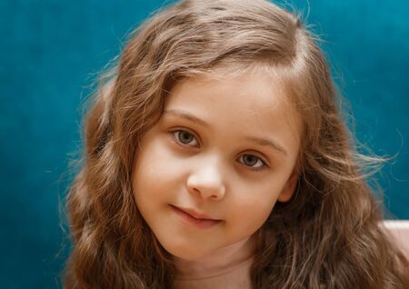 portrait of a pensive little girl with long hair on a blue background