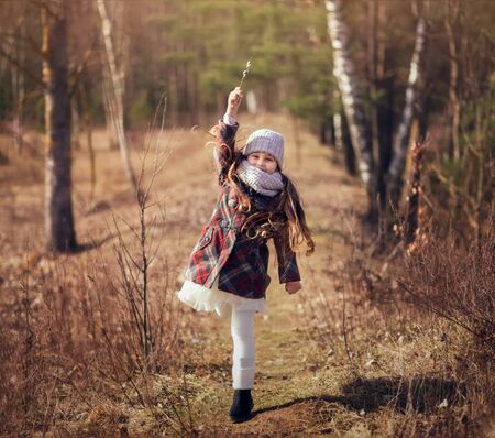 little cute girl in a coat runs along a forest pathの写真素材