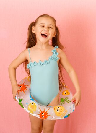 little cute girl in a swimsuit and with a rubber ring on a pink backgroundの写真素材