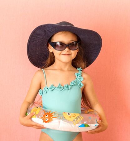 little cute cheerful girl in a swimsuit, hat and glasses on a backgroundの写真素材