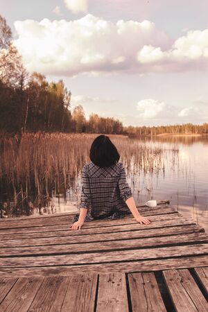 rear view of a young cute girl sitting on a pierの写真素材