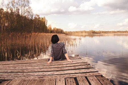 rear view of a young cute girl sitting on a pierの写真素材