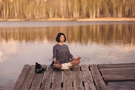 young cute girl sits on a pier in a summer dressの写真素材