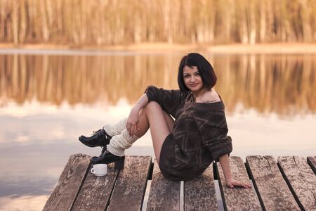 young cute girl with short hair sits on a pier in the summerの写真素材