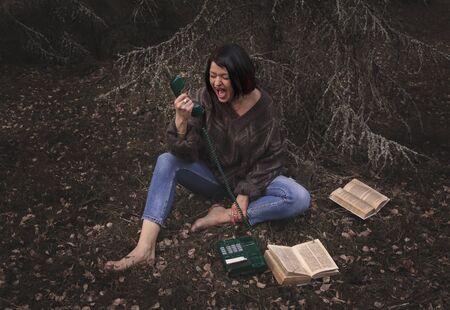 young woman screams into a telephone receiver in nature in summerの写真素材
