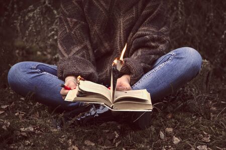 young woman sets fire to a book in natureの写真素材