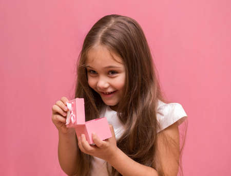 little girl joyful opens a gift box on a pink background