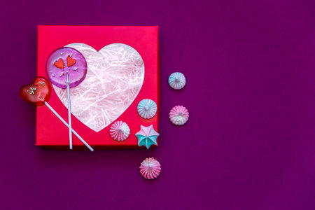 Box with hearts on a purple background. Lollipops and sweets. Composition for Valentine's Day. Copy...