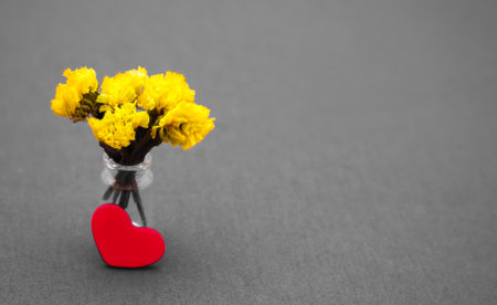 small bunch of yellow flowers and a red heart on a gray background. Valentine's day
