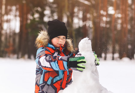 Boy sculpts snowman in winter in the woods on a sunny dayの写真素材