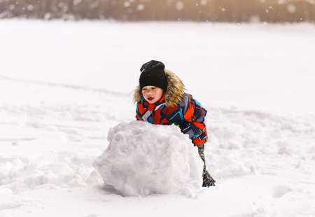 Little boy sculpts a snowball in winter in the park.