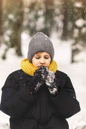 A teenage boy drinks hot tea in the winter forest. Colors 2021の写真素材