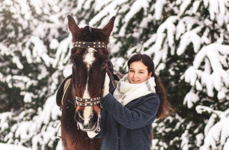 Cute teenage girl in coat with horse winter in the woodsの写真素材